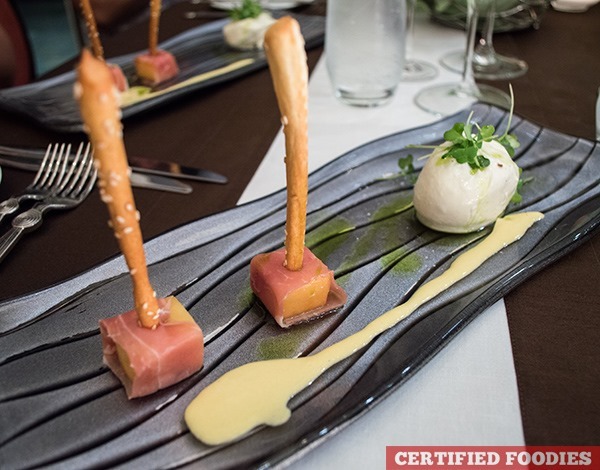 Prosciutto-wrapped melon with homemade bread sticks and imported Burrata cheese topped with micro arugula
